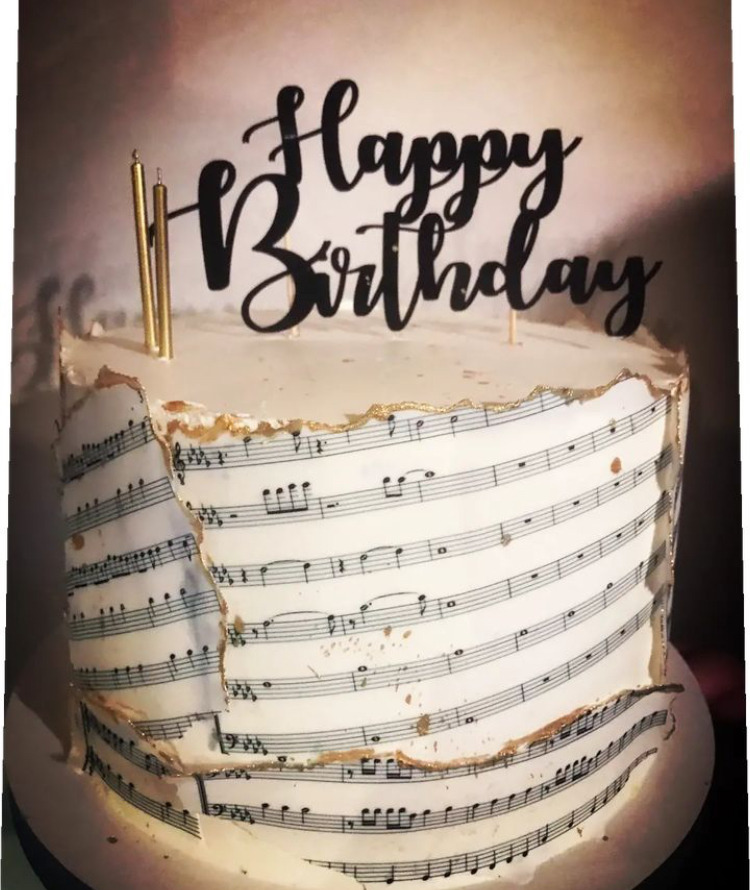 Tort urodzinowy z motywem nut, złotymi świeczkami i napisem 'Happy Birthday'. Dekoracja z jadalnego papieru nutowego, delikatne złote akcenty na brzegach.