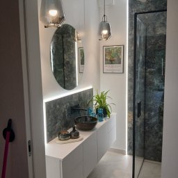 Pat-Bud - Nowoczesna łazienka z owalnym lustrem, marmurową ścianą i szklaną kabiną prysznicową. Minimalistyczne oświetlenie i rośliny dodają wnętrzu elegancji.