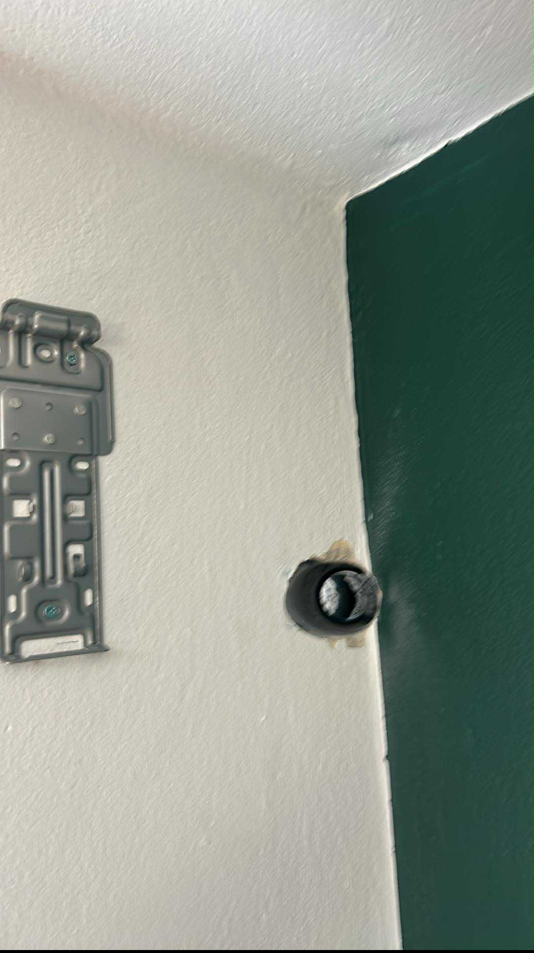 Przygotowanie otworu i montaż wspornika klimatyzacji na ścianie pomalowanej na biało i zielono, widoczne elementy instalacji.