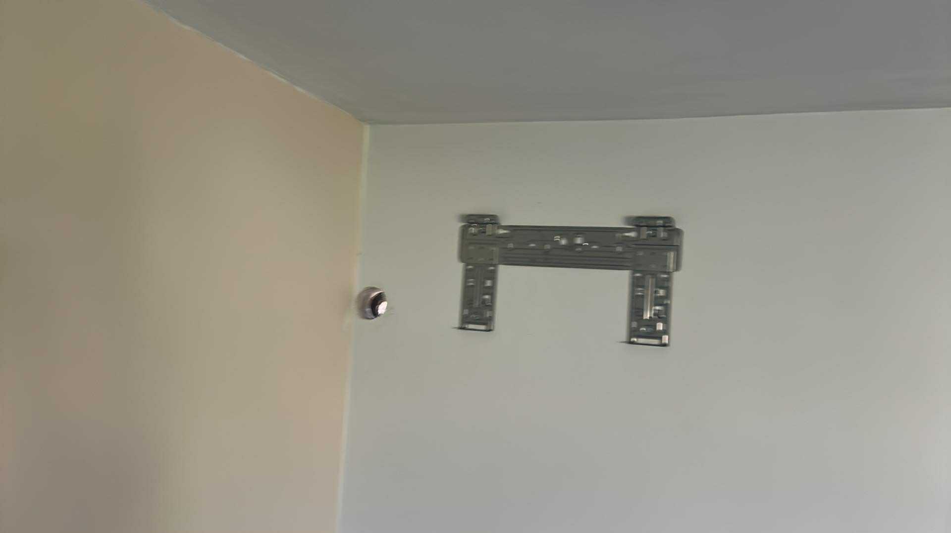 Metalowy uchwyt klimatyzatora zamontowany na białej ścianie, obok widoczny otwór na instalację. Przygotowanie do montażu jednostki wewnętrznej.