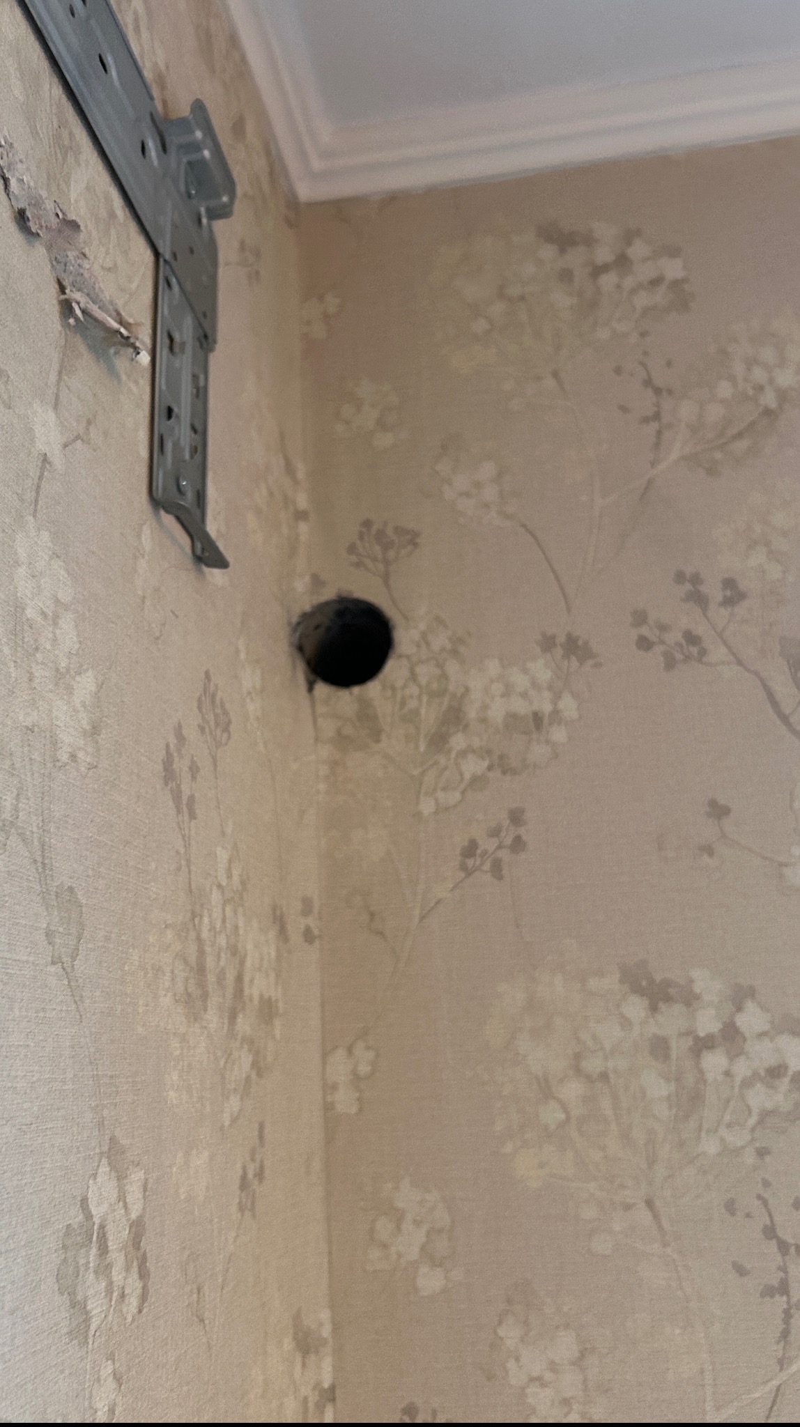 Montaż klimatyzacji: uchwyt na ścianie z wywierconym otworem na rury instalacyjne. Tapeta w kwiaty w tle.