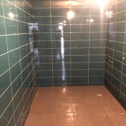 PROremont - Wykończona łazienka z ciemnozielonymi płytkami ściennymi i brązowymi płytkami podłogowymi. Widoczne otwory na armaturę i rury.