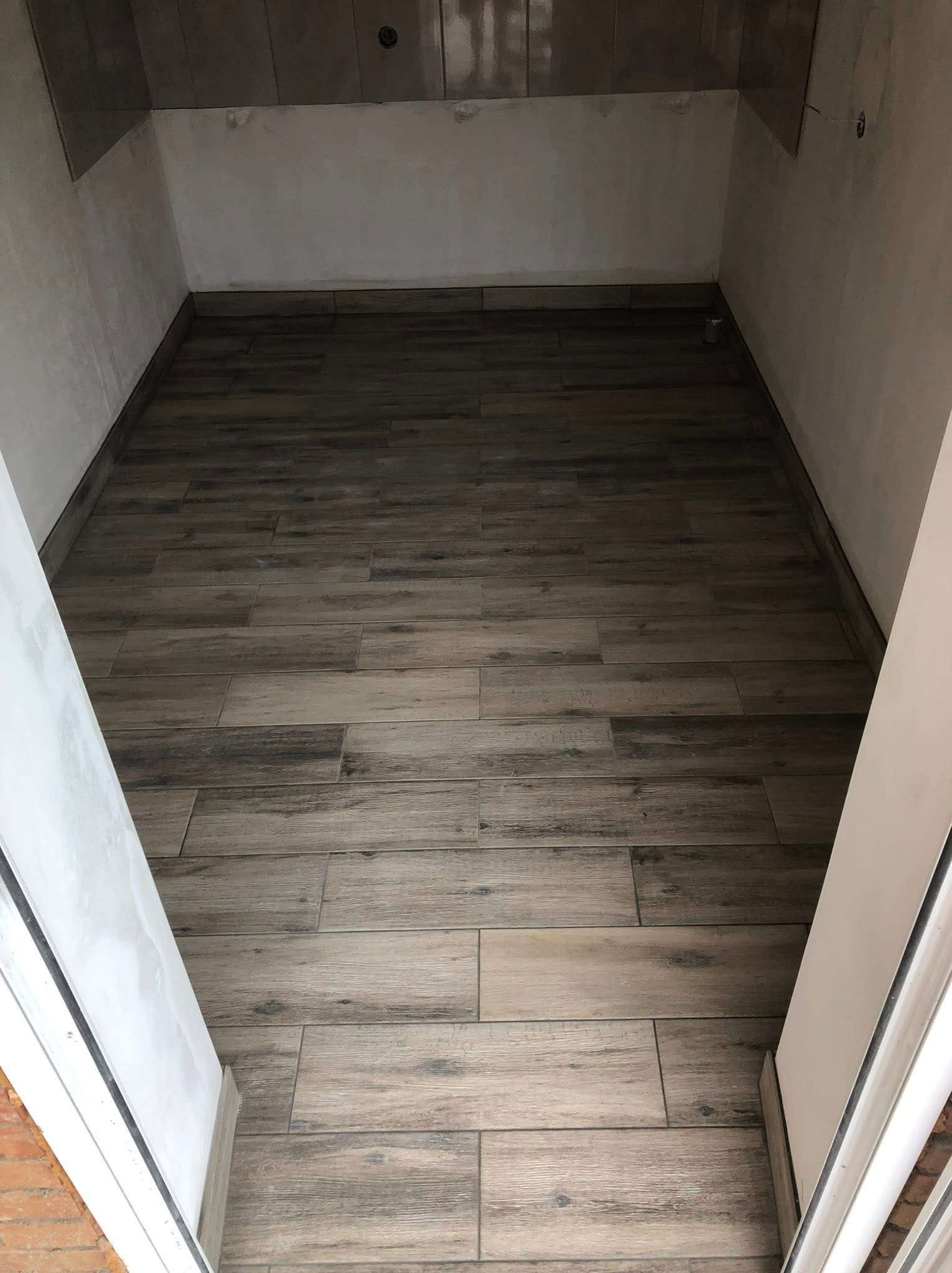 Ułożona podłoga z płytek imitujących drewno w małym pomieszczeniu we Wrocławiu. Widoczne fugi i fragmenty ścian przygotowanych do dalszych prac.