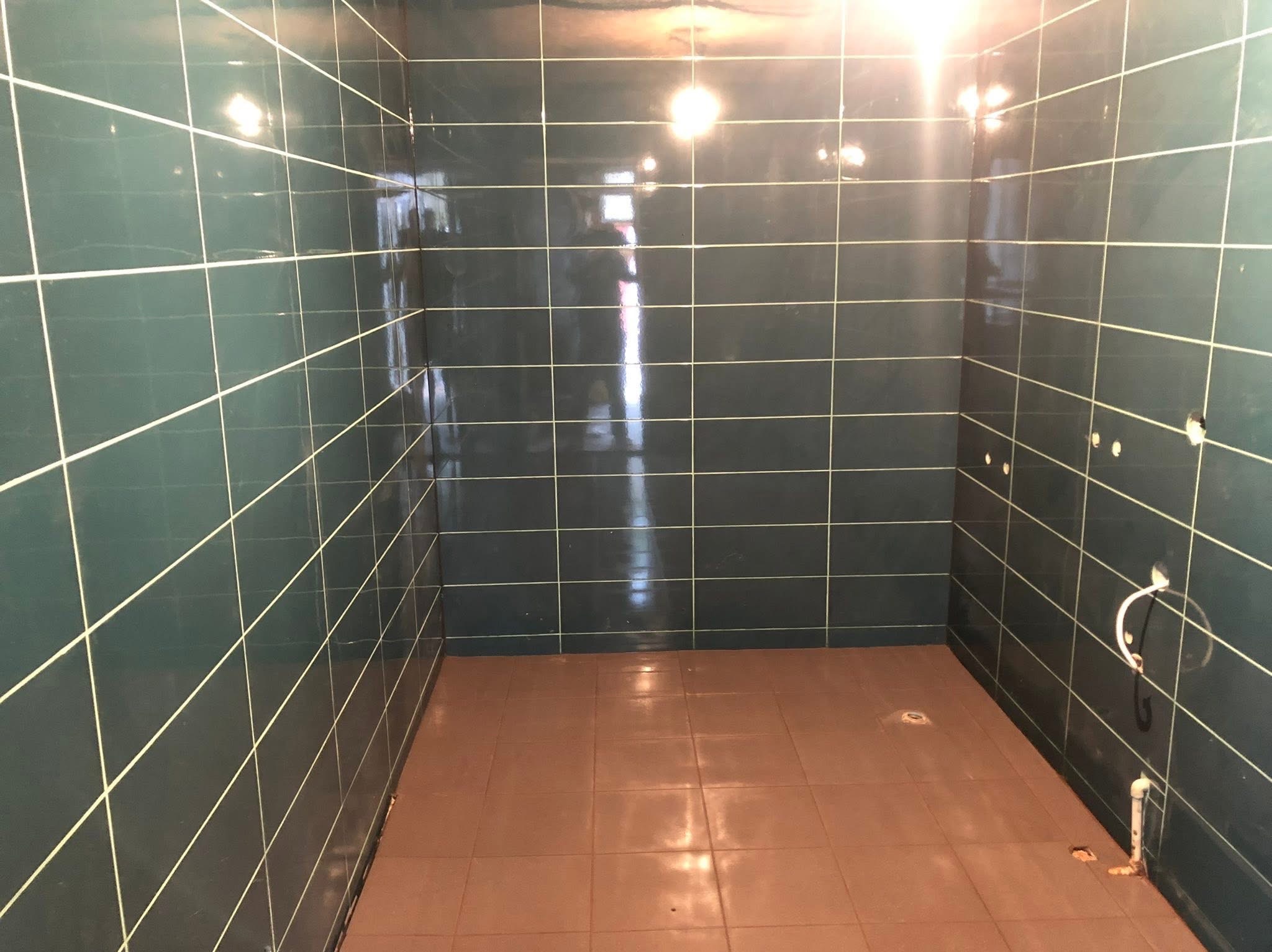 Wykończona łazienka z ciemnozielonymi płytkami ściennymi i brązowymi płytkami podłogowymi. Widoczne otwory na armaturę i rury.