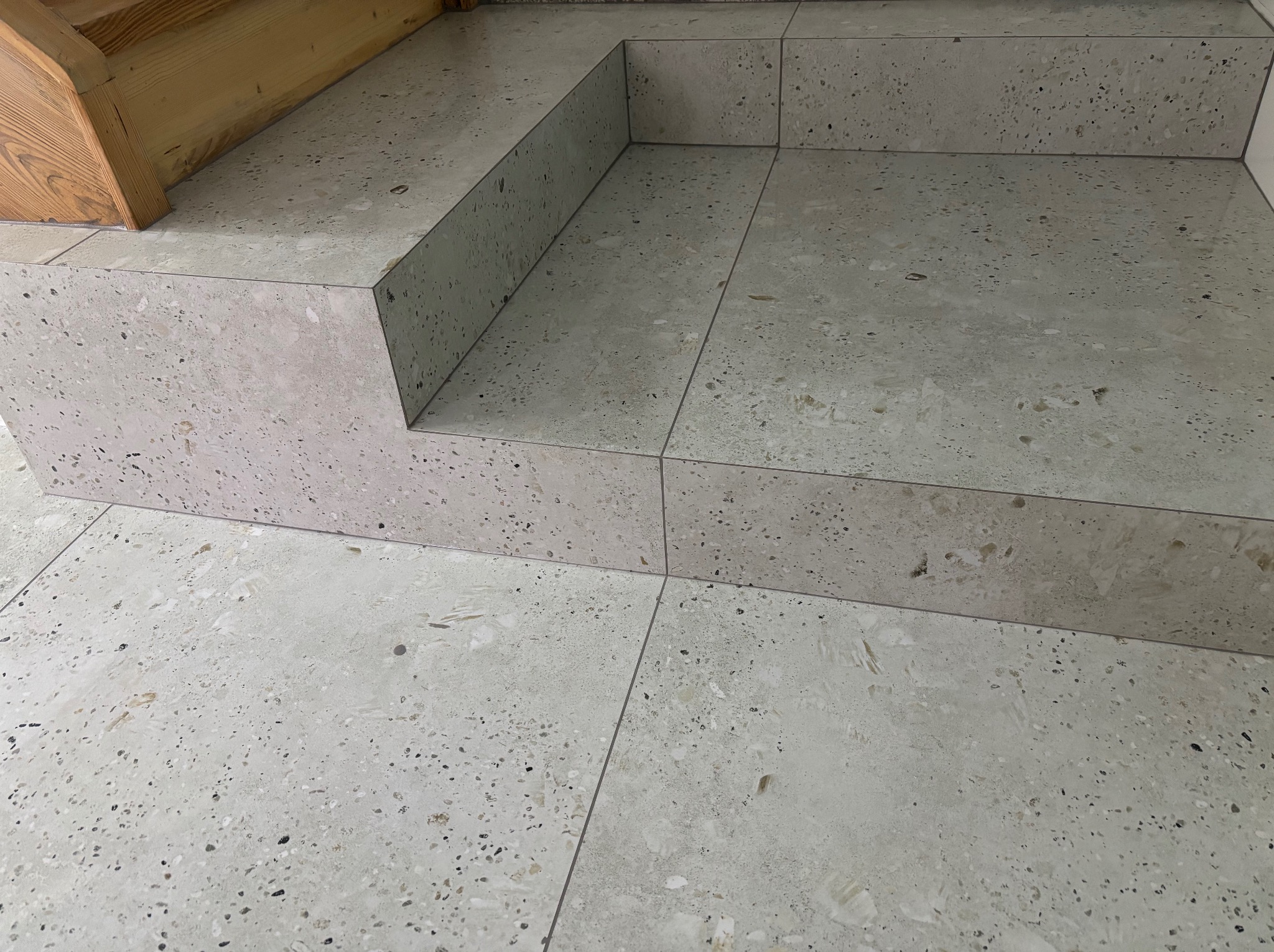 Schody wyłożone jasnymi płytkami lastryko z widocznymi spoinami, drewniany element u góry, nowoczesny design.