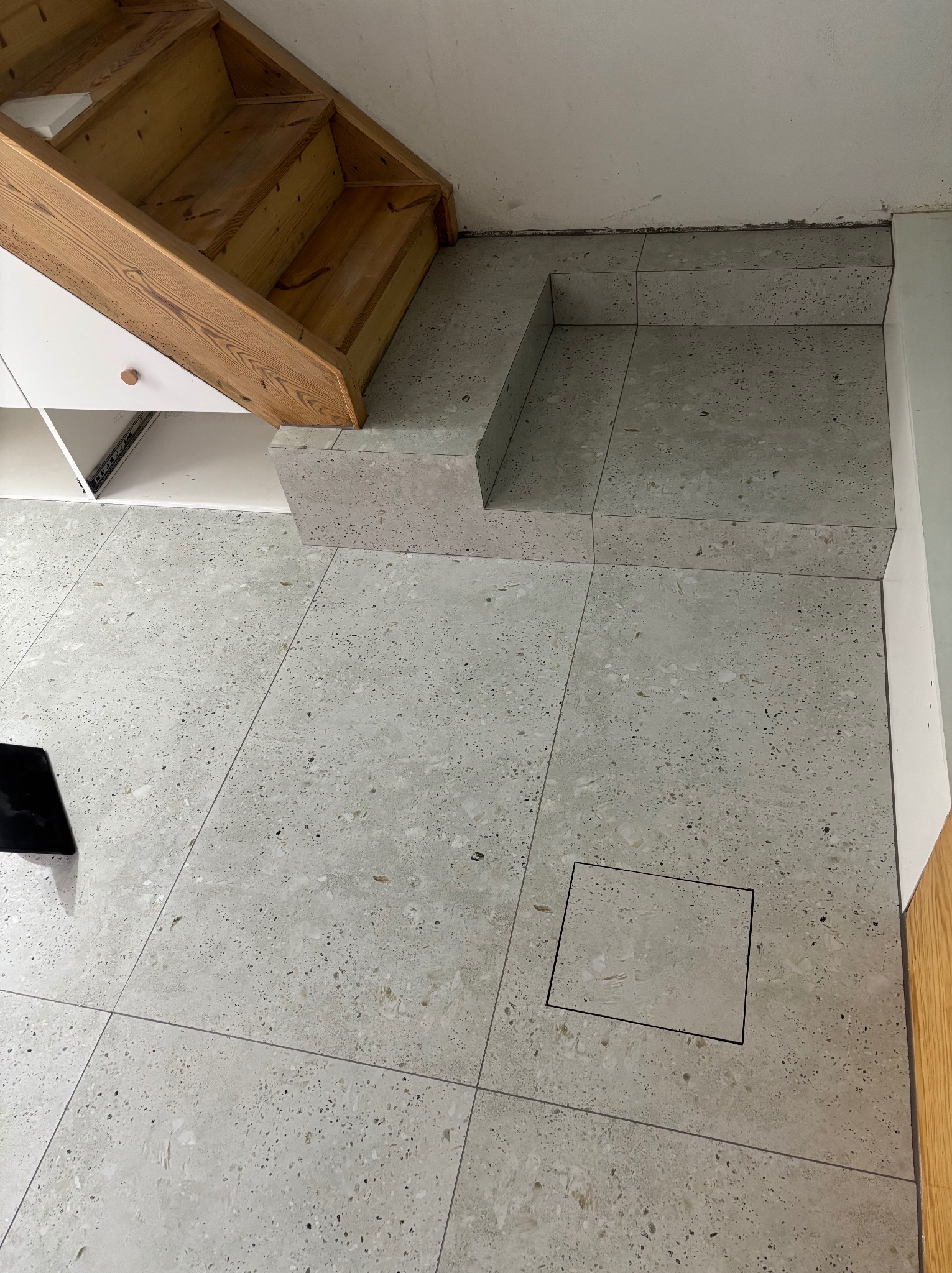 Wykończona podłoga z płytek lastryko w odcieniach szarości, z widoczną drewnianą konstrukcją schodów i zabudową szafki. Uwagę zwraca precyzyjne ułożenie płytek.