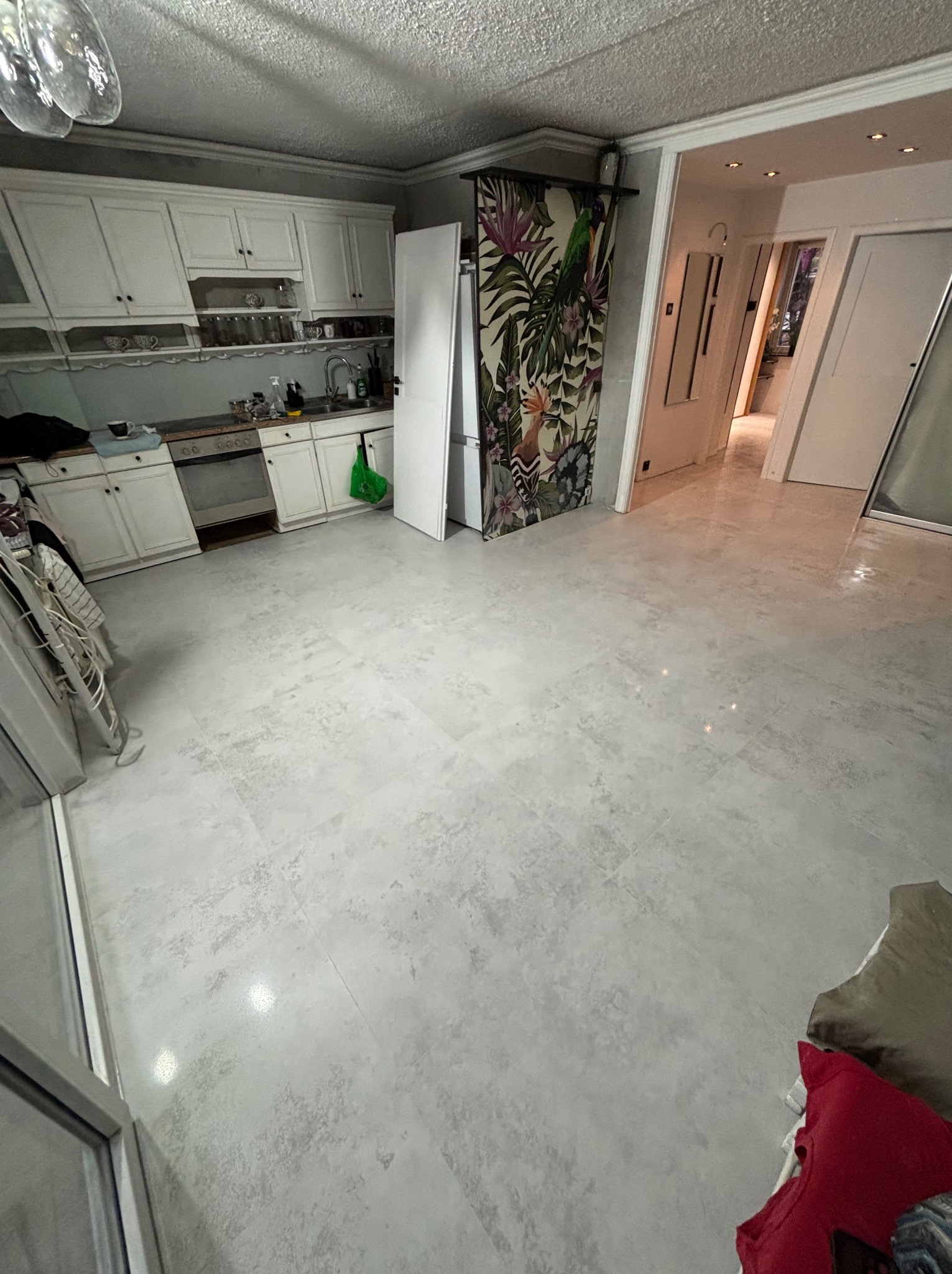 Jasnoszara, matowa podłoga z płytek w wyremontowanym wnętrzu kuchni. Widoczne białe szafki kuchenne i drzwi z motywem roślinnym. Nowoczesne oświetlenie.