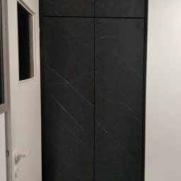 Piotr Kołosowski - Czarna szafa wnękowa z subtelnym wzorem marmuru, wkomponowana w wąskie pomieszczenie, widoczna obok białych drzwi.