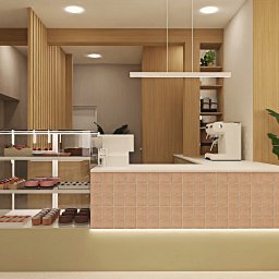 Bjorn Studio Karolina Strzelczyk - Wnętrze kawiarni z ladą wykończoną mozaiką, przeszkloną witryną z ciastami i ekspres do kawy. Elementy drewniane i rośliny doniczkowe dopełniają aranżację.