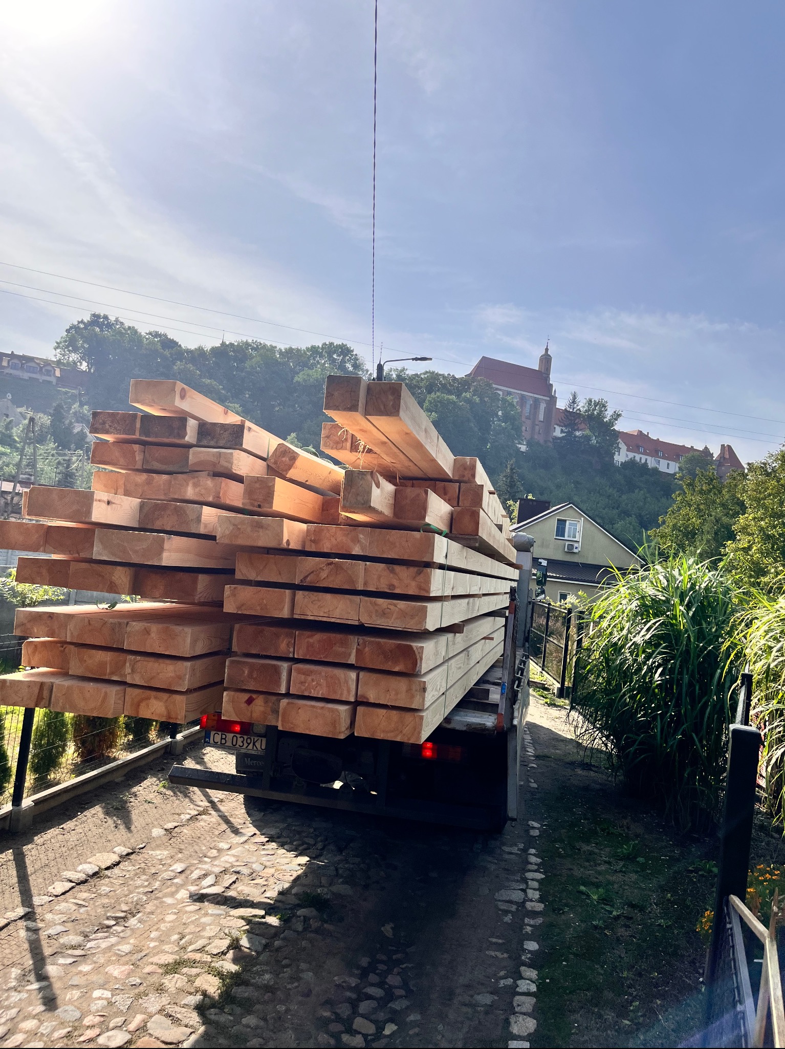 Transport tarcicy na ciężarówce z widokiem na miasto i kościół w tle. Ułożone drewno budowlane w słoneczny dzień. Widok z tyłu pojazdu.