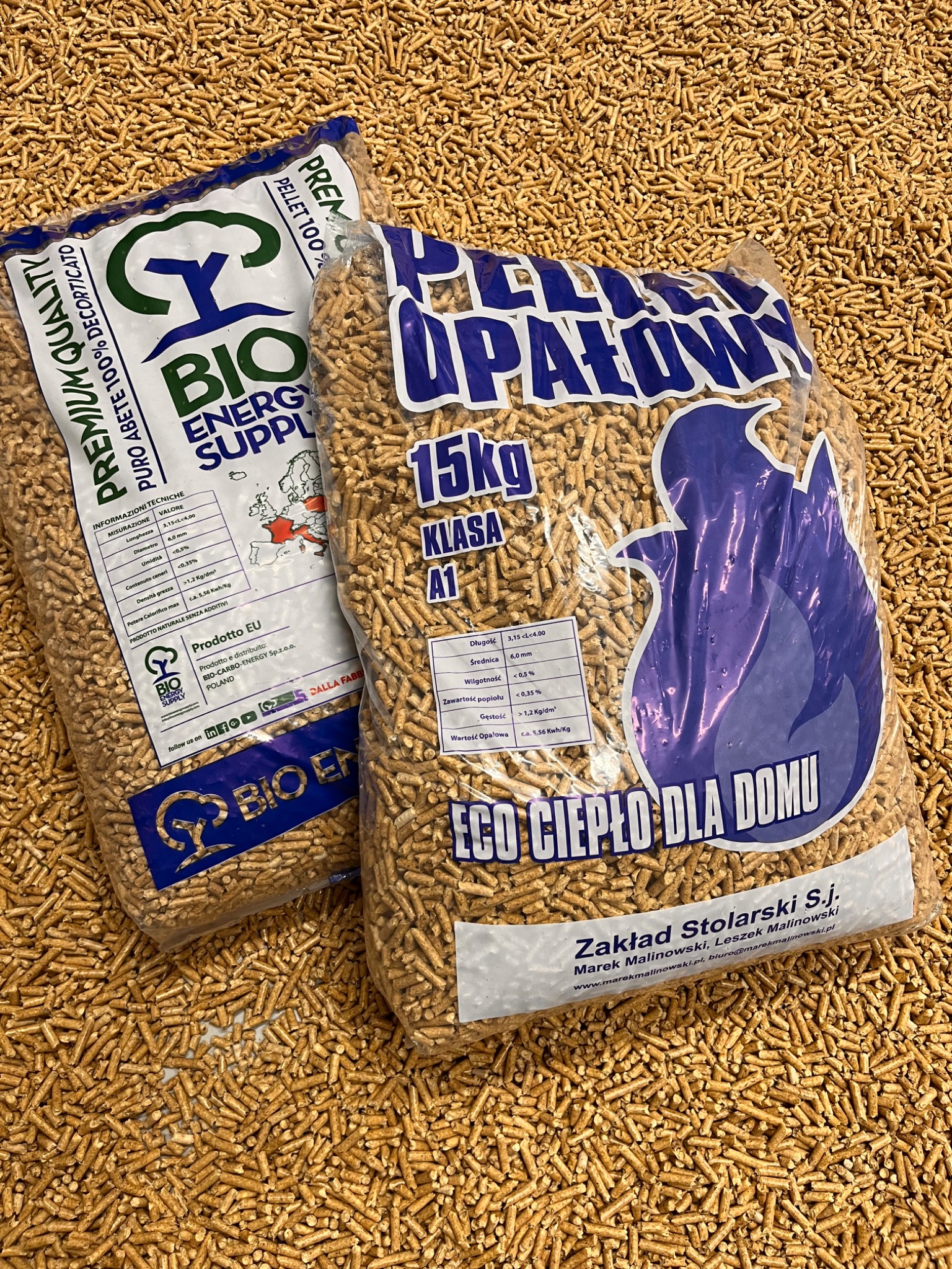 Dwa worki pelletu drzewnego klasy A1, jeden z napisem 'Bio Energy Supply', drugi 'Eco Ciepło dla domu', na tle rozsypanego pelletu. Widoczne dane techniczne.