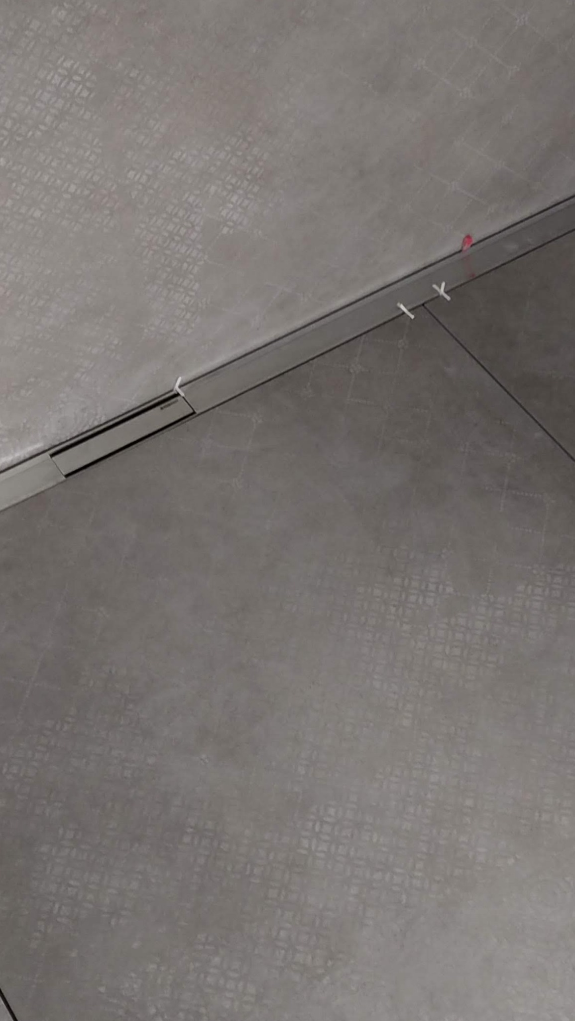 Ułożone szare płytki podłogowe z delikatnym wzorem, widoczne listwy przypodłogowe i elementy dystansowe, świeżo po montażu.