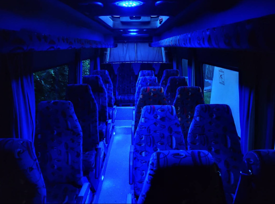 Wnętrze autobusu w Lubartowie z niebieskim oświetleniem LED, widok na fotele z wzorzystą tapicerką. Klimatyczne oświetlenie tworzy unikalny nastrój w pojeździe.