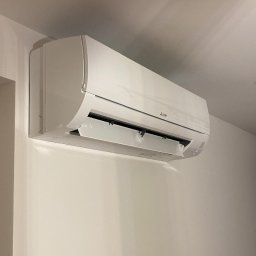 ELEKTRO - Dariusz - Biała klimatyzacja Mitsubishi zamontowana na ścianie, widoczna z boku, z otwartą klapką. Minimalistyczny design, jasne wnętrze, neutralne tło.