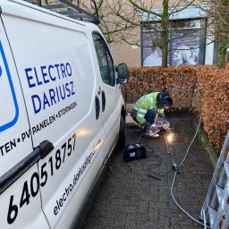 ELEKTRO - Dariusz - Pracownik w kombinezonie spawalniczym spawa metalową konstrukcję na zewnątrz, obok firmowego busa z napisem 'Electro Dariusz' i numerem telefonu.