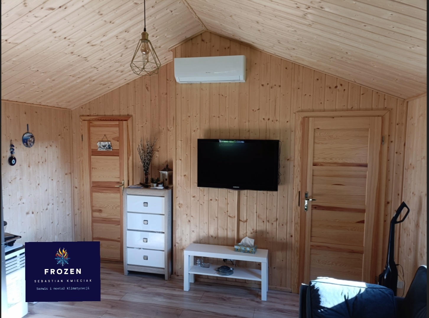 Klimatyzator ścienny zamontowany w drewnianym wnętrzu domu w Środzie Wielkopolskiej, widoczne drzwi i meble. Oświetlenie sufitowe w stylu industrialnym.