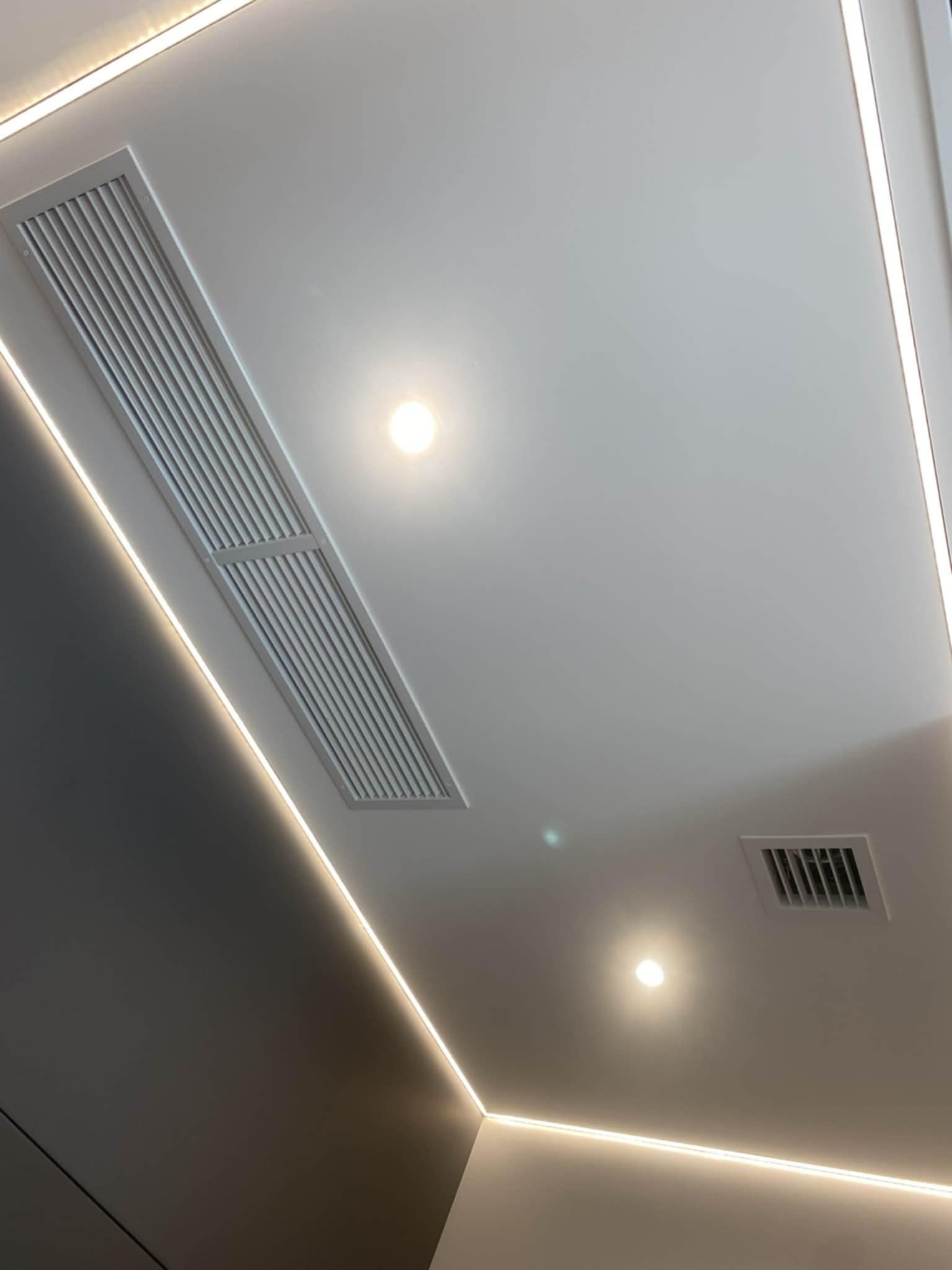 Nowoczesny sufit podwieszany z oświetleniem LED i kratkami wentylacyjnymi. Minimalistyczny design, precyzyjne wykończenie, równomierne światło.