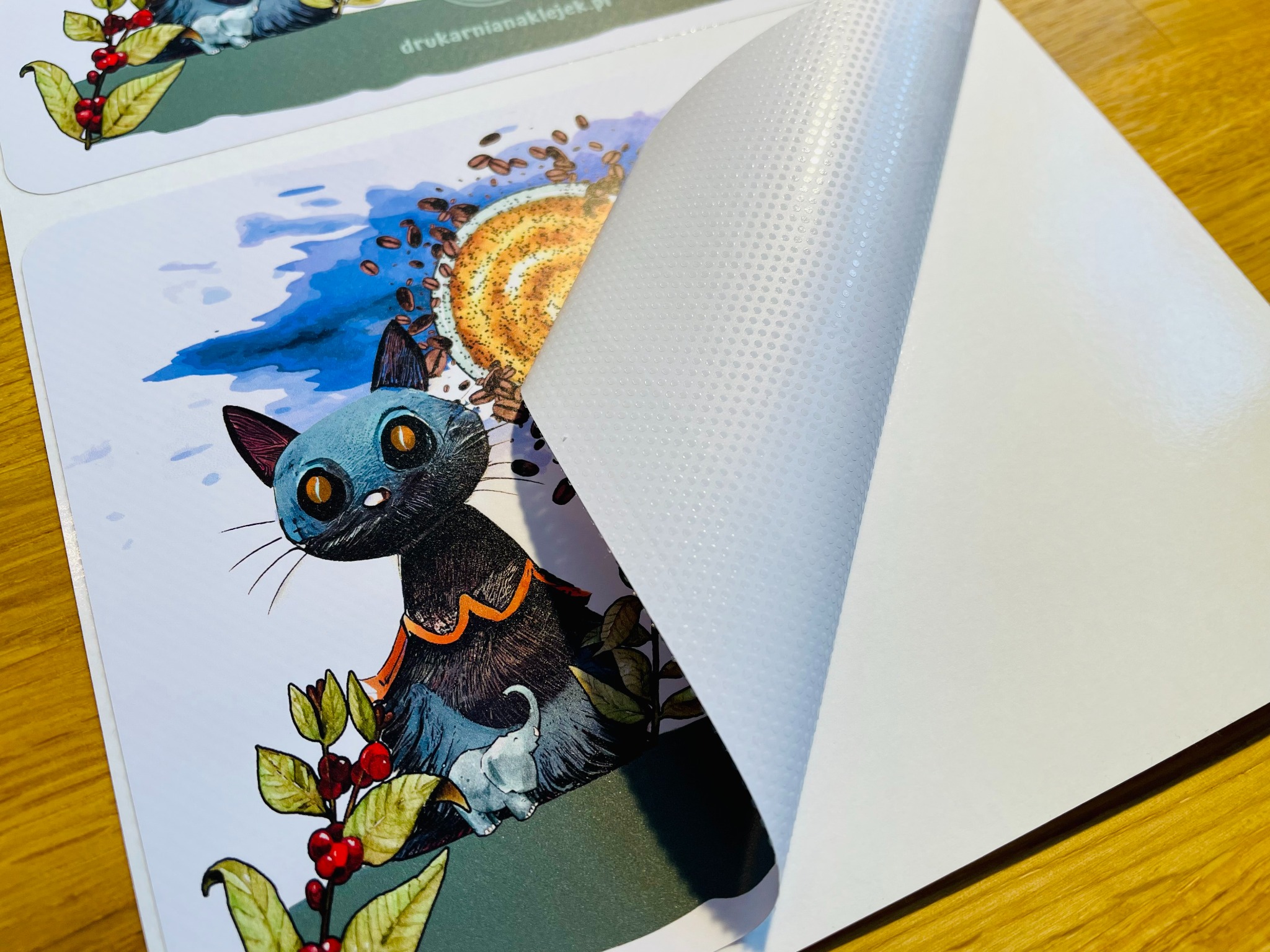 Arkusz z ilustrowanymi naklejkami, częściowo odklejony od podkładu, prezentujący druk pełnokolorowy z motywem kota, kawy i słonia na matowej folii z klejem punktowym.