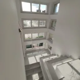 Białe schody z marmurowym wzorem w jasnym, nowoczesnym wnętrzu z oknami na kilku poziomach. Widok z góry.