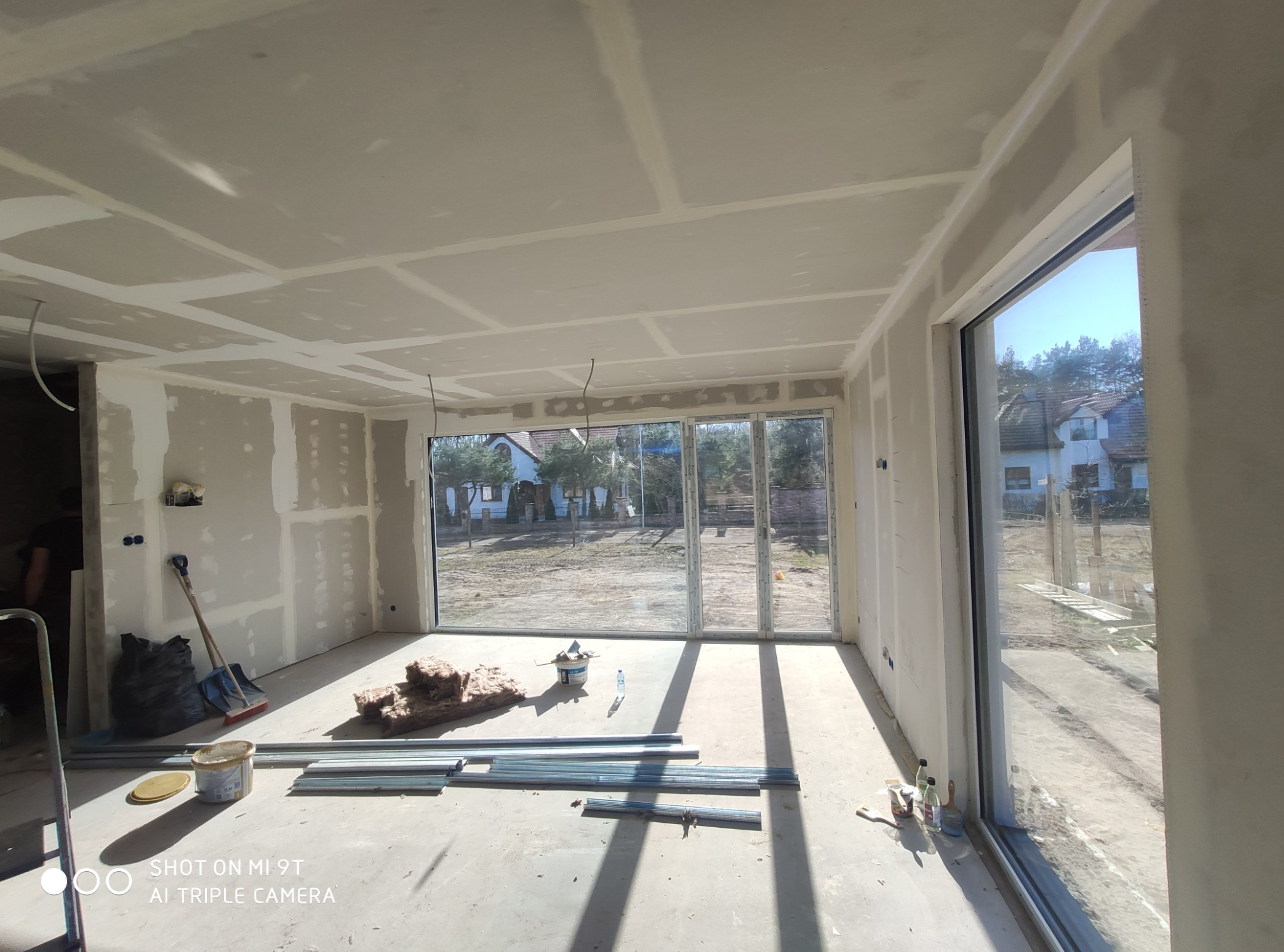 Wnętrze w trakcie prac w Słupsku: ściany i sufit z płyt karton-gips, widoczne profile, ocieplenie, szpachlowanie. Duże okno z widokiem na zewnątrz.