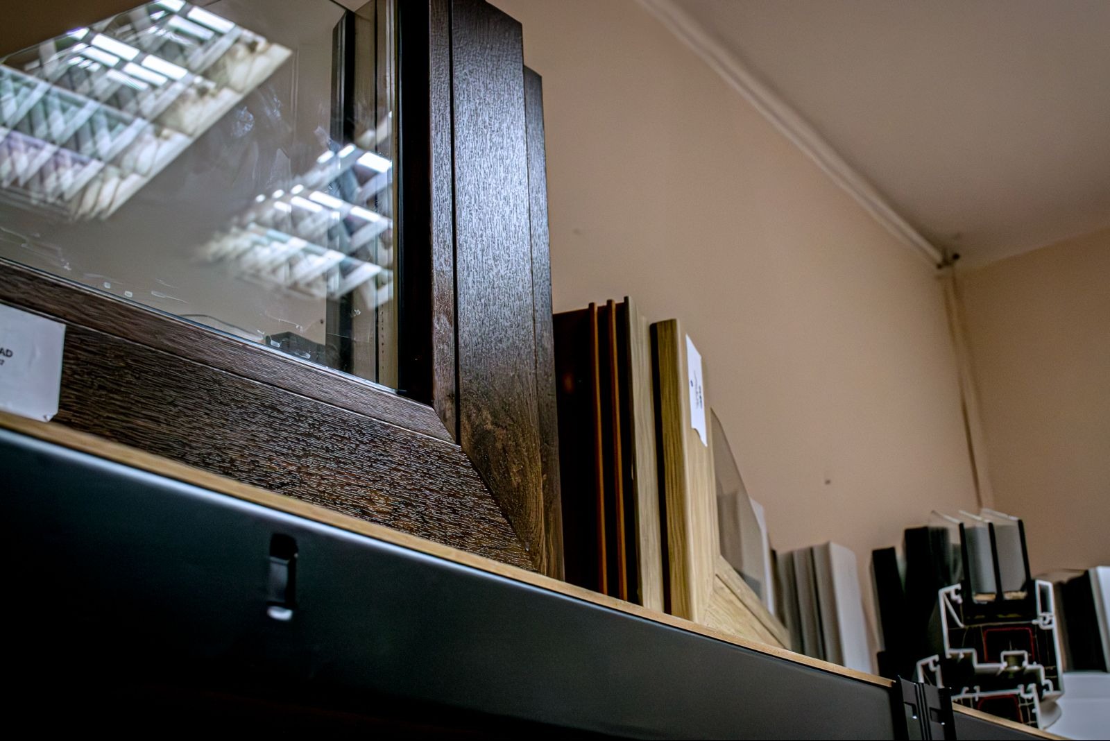 Ekspozycja przekrojów ram okiennych w różnych kolorach i fakturach drewna, prezentowana w Nysie. Widoczne detale wykończenia i konstrukcji.