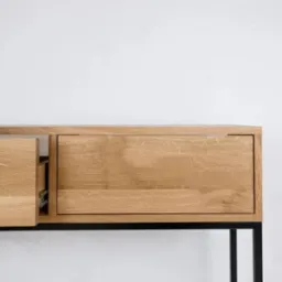 Minimalistyczna komoda z dębowego drewna na czarnych, metalowych nogach. Jedna szuflada wysunięta, ukazująca prowadnice. Jasne, naturalne wykończenie drewna.