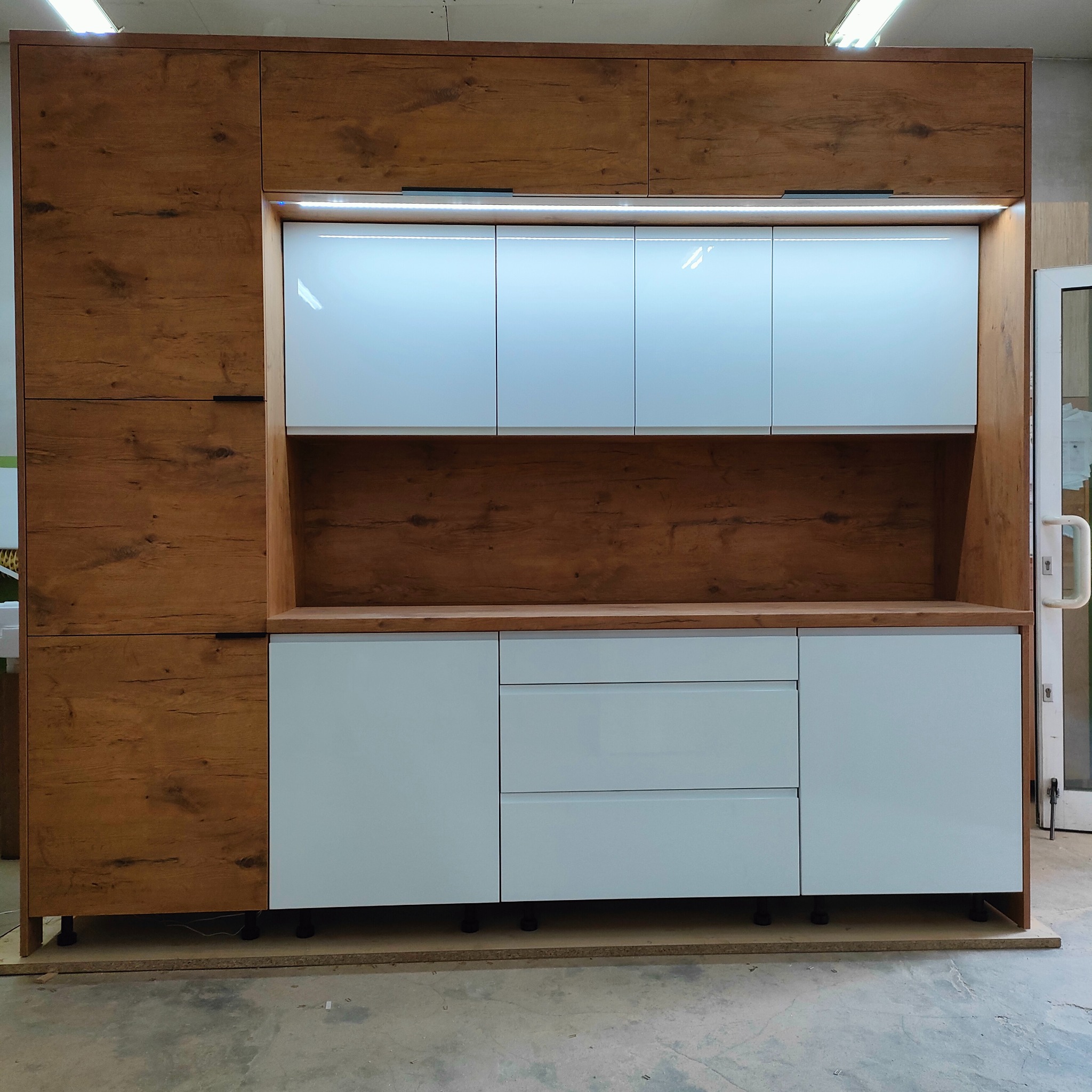 Nowoczesna zabudowa kuchenna: połączenie matowych, błękitnych frontów i drewnopodobnych, brązowych korpusów. Górne szafki z oświetleniem LED.