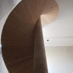 Spiralne schody drewniane, widok od dołu, ukazujące unikalną konstrukcję i naturalne wykończenie. Jasne drewno i minimalistyczny design.