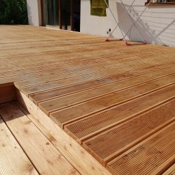 CLIC HOUSE WOOD - Nowy taras z desek ryflowanych, z widocznym stopniem i suszarką na pranie w tle, prezentowany w słoneczny dzień.