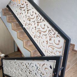 CLIC HOUSE WOOD - Nowoczesna balustrada schodowa z ażurowym, białym wypełnieniem i czarną ramą, widok z dołu na schody wyłożone płytkami imitującymi drewno.