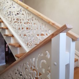 CLIC HOUSE WOOD - Białe schody z ozdobną, ażurową balustradą i drewnianymi poręczami, widziane z dołu pod kątem, prezentujące detale wykończenia.