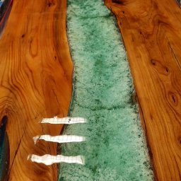 CLIC HOUSE WOOD - Blat stołu z drewna z żywicą epoksydową w kolorze turkusowym, imitującą rzekę. Widoczne słoje drewna i refleksy świetlne na powierzchni żywicy.