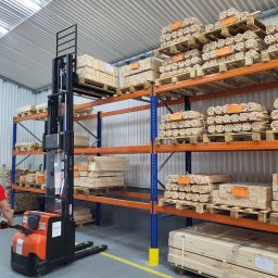CLIC HOUSE WOOD - W magazynie operator wózka widłowego podnosi paletę z drewnianymi elementami na regał. Widoczne zapasy materiałów do produkcji drewnianych konstrukcji.