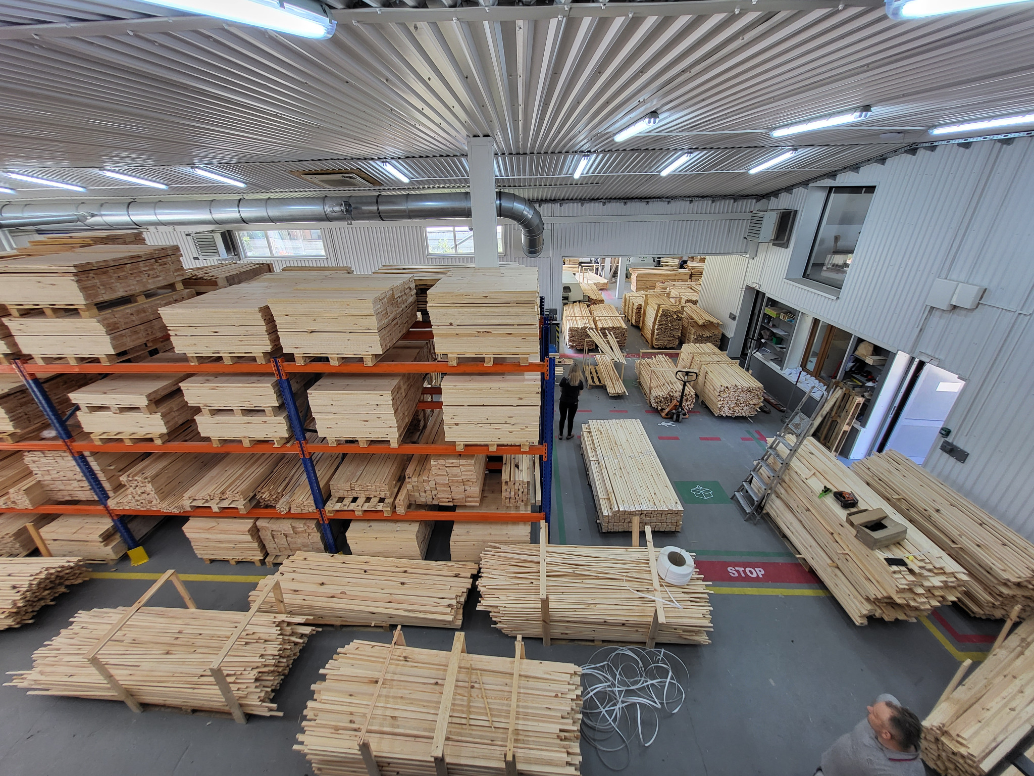 Magazyn tarcicy w Kroczycach: liczne stosy obrobionego drewna na regałach i podłodze, przygotowane do dalszej obróbki. Widok z góry na halę produkcyjną.