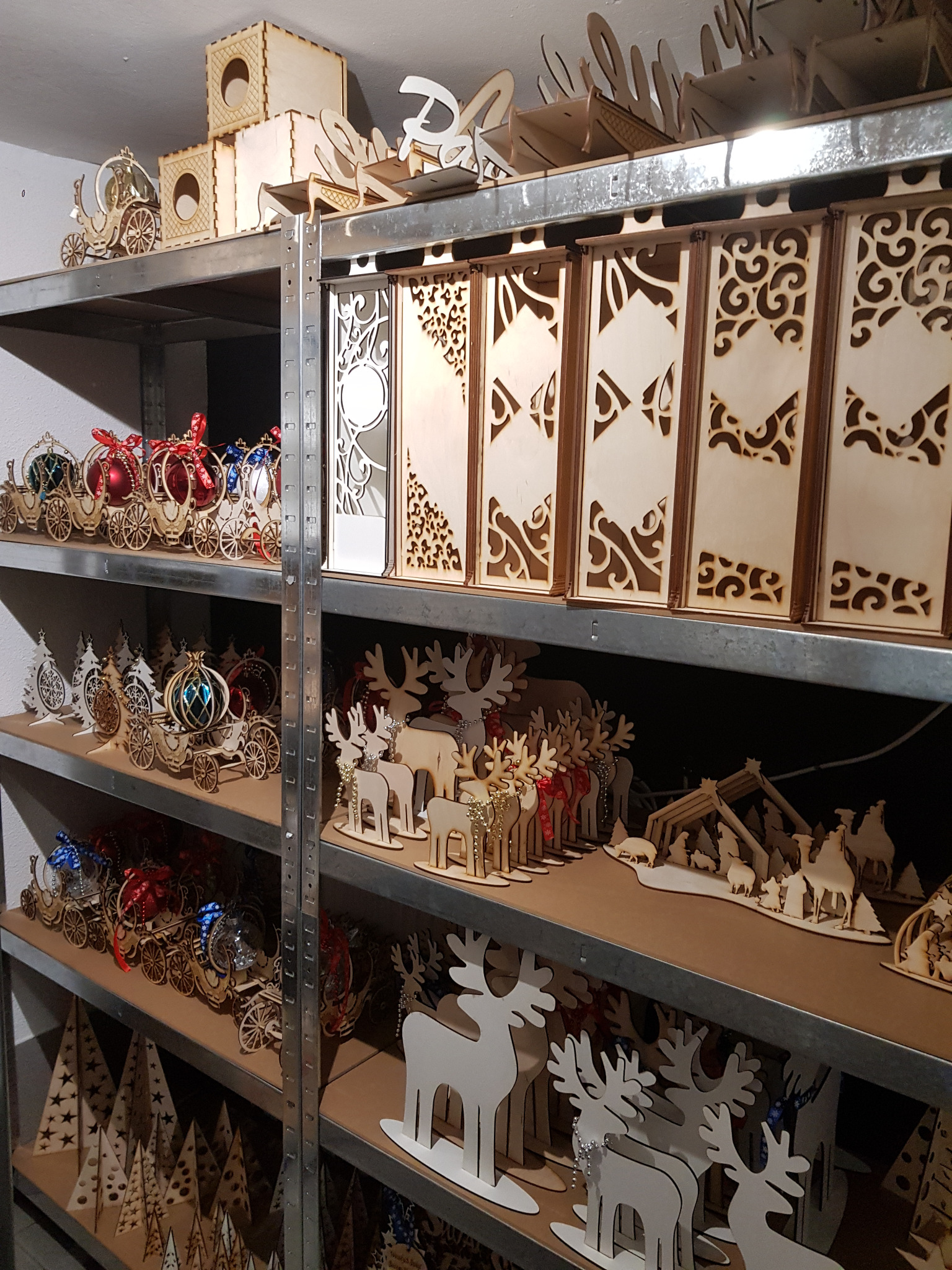 Regał z drewnianymi ozdobami: wycinane laserowo renifery, choinki, karoce z bombkami i ażurowe panele, tworzące bożonarodzeniowy asortyment stolarski.