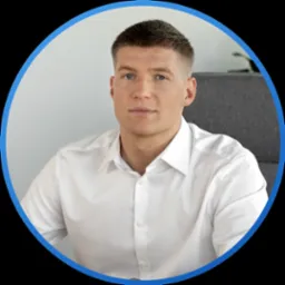 Portret młodego mężczyzny w białej koszuli, siedzącego na szarym krześle, na neutralnym tle, w niebieskim okręgu kadrującym.