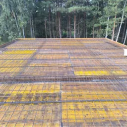 Żółte szalunki Doka 3-SO z ułożonym zbrojeniem na tle lasu. Widok z góry na przygotowany strop budynku w trakcie budowy.