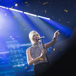 BARTŁOMIEJ SZOPA SHORE STUDIO - Piosenkarka w błyszczącej bluzce śpiewa do mikrofonu na scenie w świetle reflektorów, podczas gdy z góry opadają konfetti.