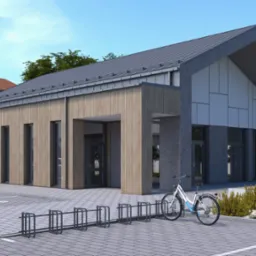 Wizualizacja budynku z drewnianą elewacją i szarą dachówką. Na pierwszym planie stojak na rowery i rower. W tle para spacerująca po chodniku, obok zaparkowany samochód.