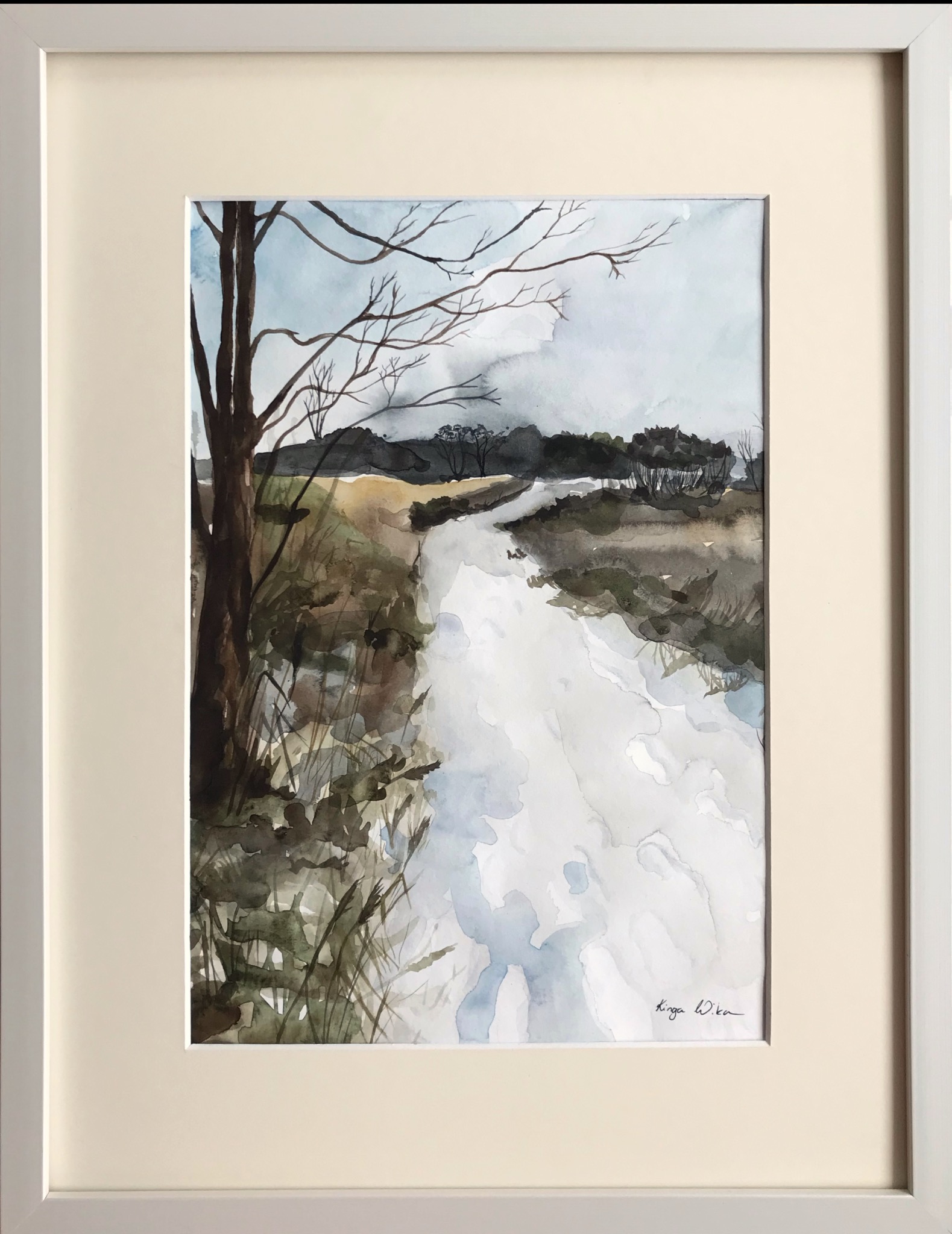 Akwarela przedstawiająca pejzaż z rzeką i drzewami, oprawiona w białą ramę z kremowym passe-partout. Widoczny podpis autora w prawym dolnym rogu.