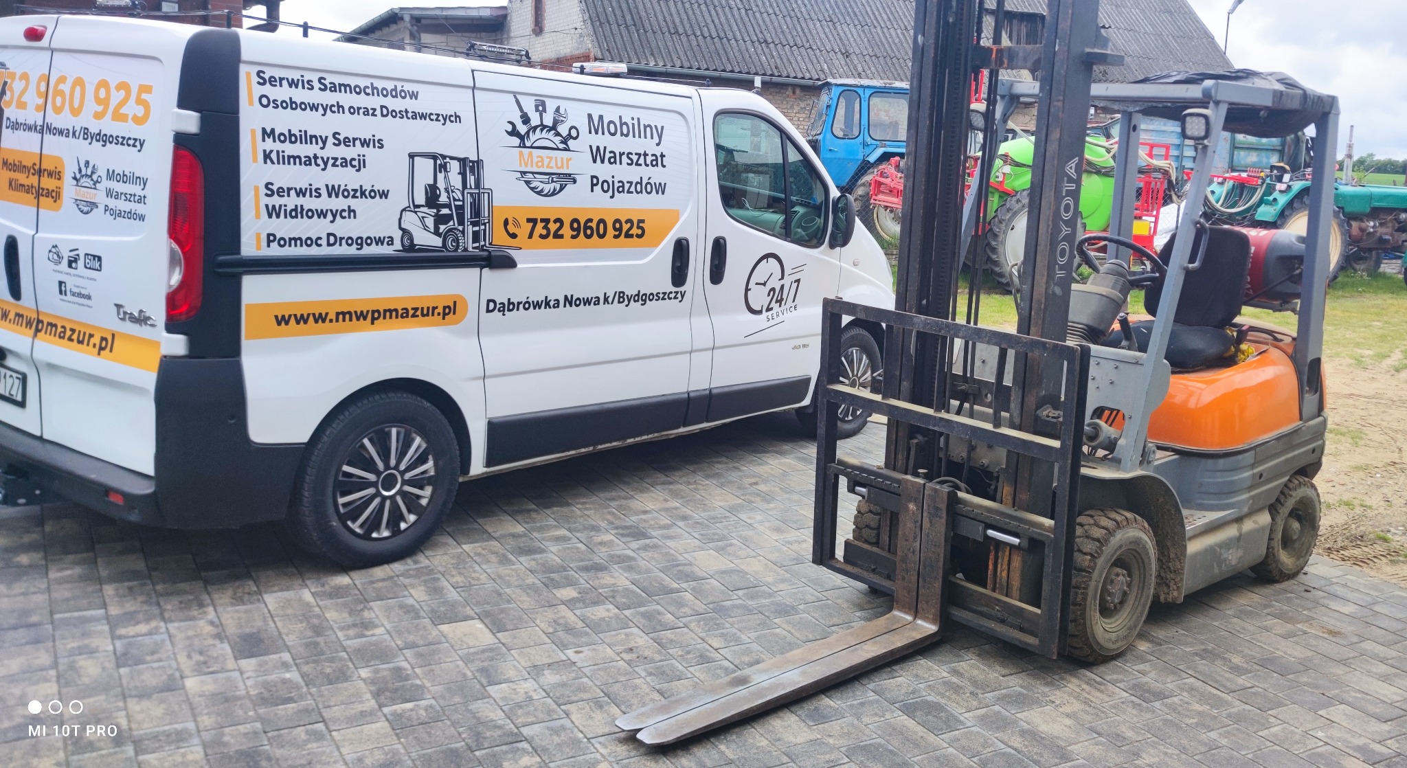 Pomarańczowy wózek widłowy Toyota na kostce brukowej, z tyłu biały bus z reklamą serwisu, w tle traktory. Dąbrówka Nowa k/Bydgoszczy, 24/7.