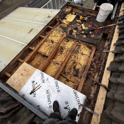 SUN-BIT Spółka z ograniczoną odpowiedzialnością - Demontaż dachu z widoczną izolacją, narzędziami i fragmentem nowego poszycia. Ujęcie z góry na remontowany dach z perspektywy osoby stojącej na nim.