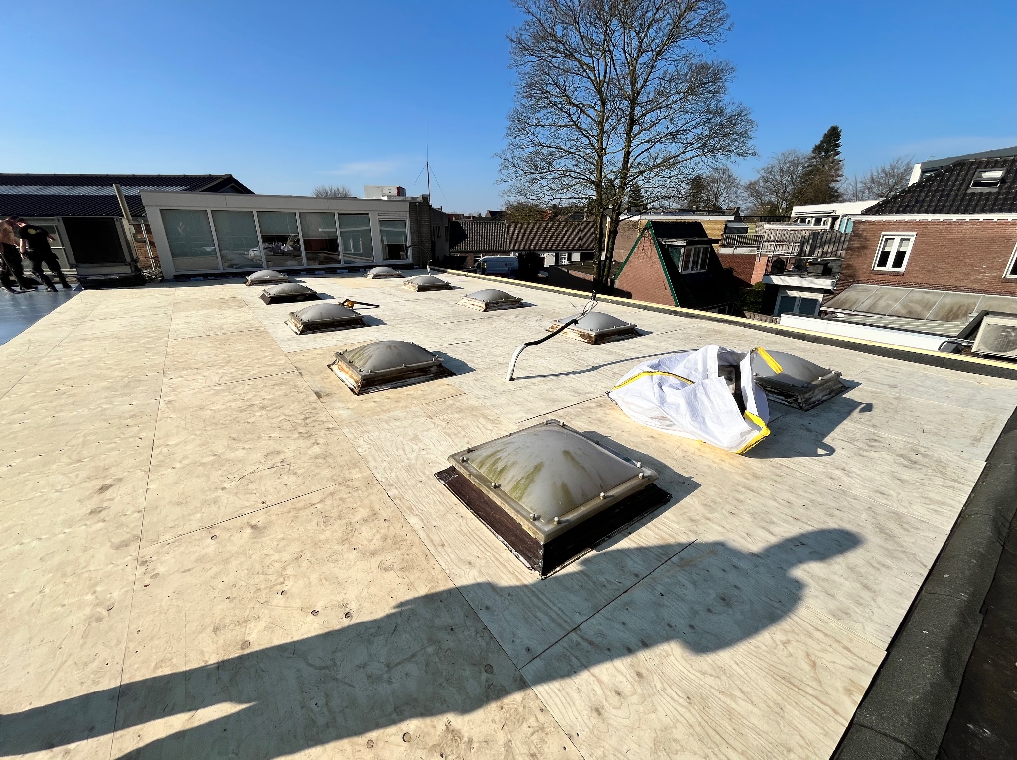 Płyta OSB na płaskim dachu z zamontowanymi świetlikami dachowymi. W tle zabudowa miejska i błękitne niebo.