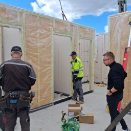 TWÓJ DOM EXPERT SPÓŁKA Z OGRANICZONĄ ODPOWIEDZIALNOŚCIĄ - Montaż modułów domu szkieletowego: ekipa budowlana w trakcie łączenia ścian z izolacją, widoczne narzędzia i elementy konstrukcyjne.