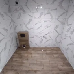 Łazienka po remoncie: ściany wyłożone białymi płytkami imitującymi marmur z szarymi żyłami, podłoga pokryta brązowymi panelami przypominającymi drewno, widoczna zabudowa podtynkowego WC...