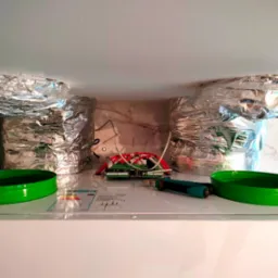 Wnętrze rekuperatora z podłączonymi przewodami wentylacyjnymi w folii aluminiowej. Widoczne elementy elektroniki i zielone pierścienie uszczelniające.