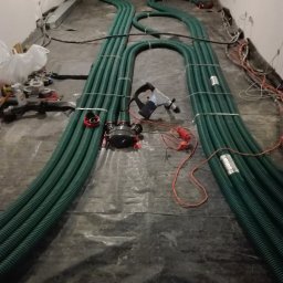 NOVUM-INSTAL - Układanie zielonych rur wentylacyjnych na podłodze, widoczne narzędzia i elementy instalacji. Etap montażu rekuperacji w pomieszczeniu.