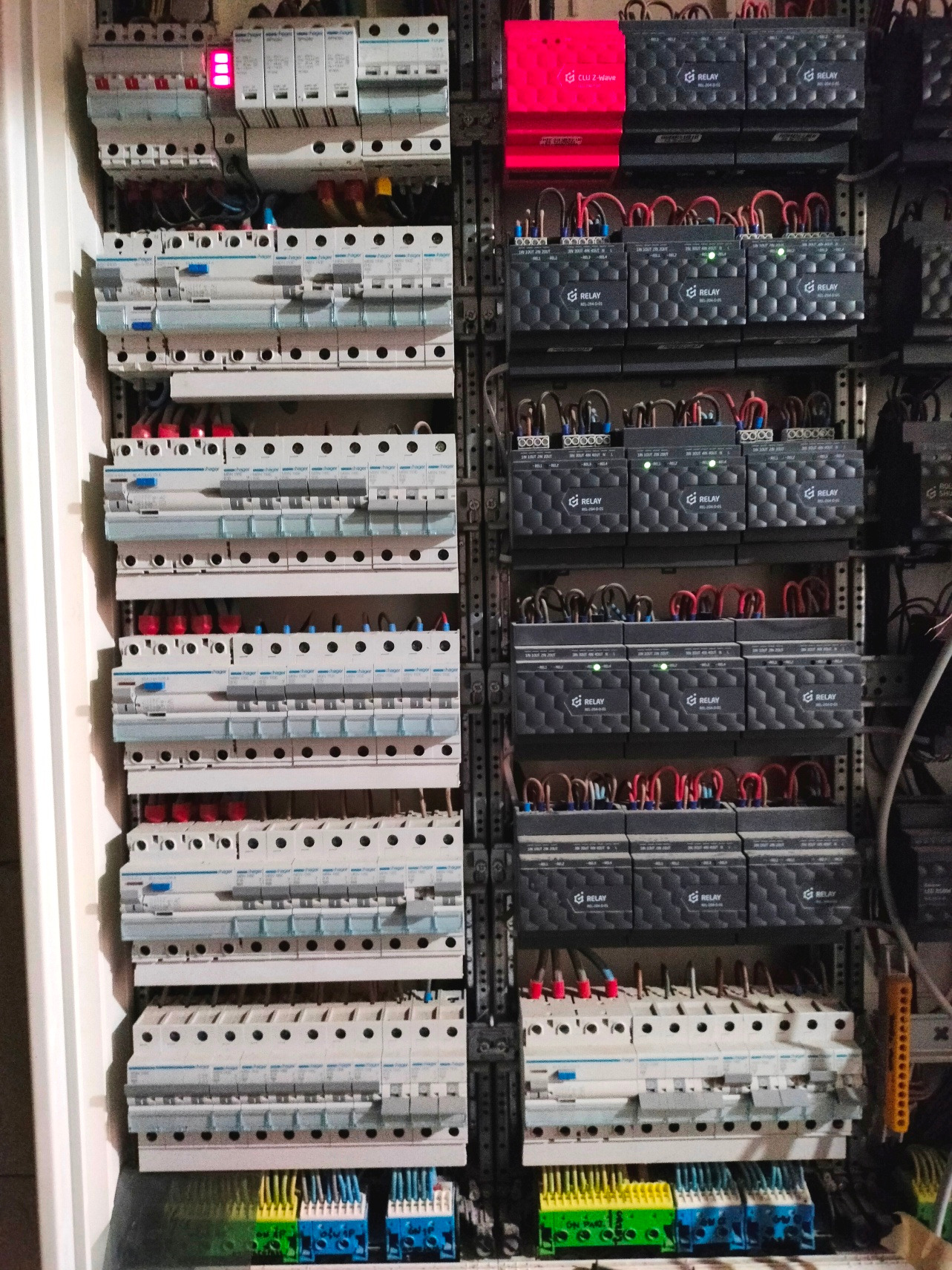 Panel sterowania z licznymi bezpiecznikami i modułami przekaźnikowymi. Widoczne przewody i elementy instalacji elektrycznej. Różne kolory przewodów i modułów.