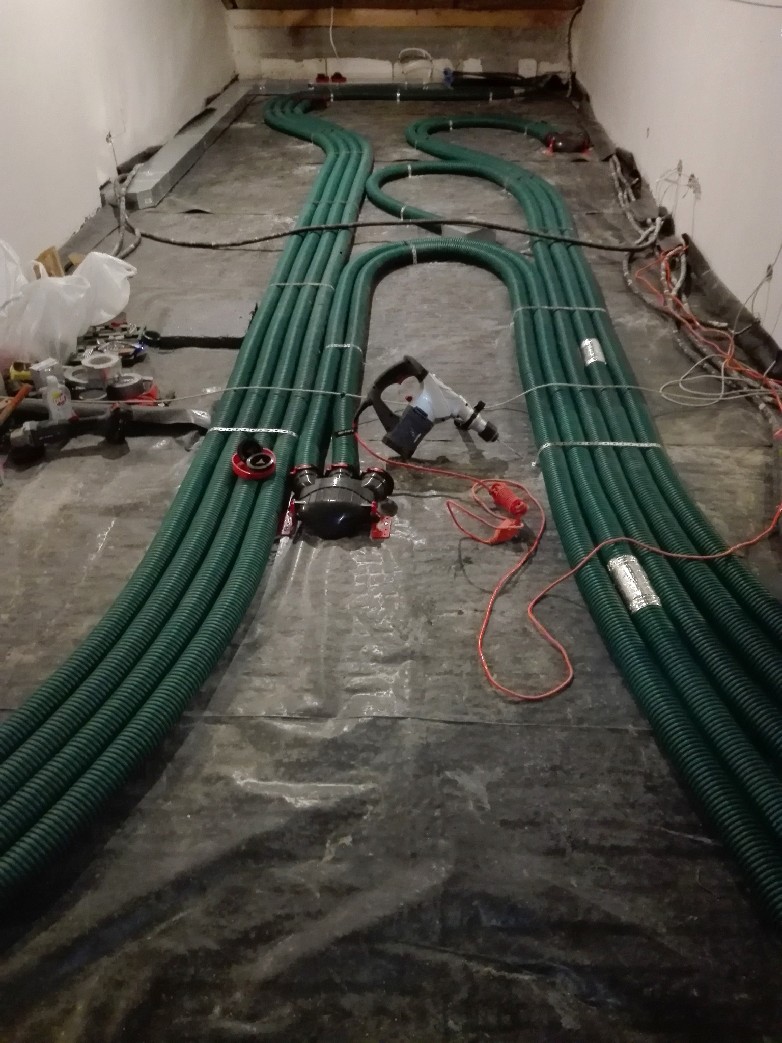 Układanie zielonych rur wentylacyjnych na podłodze, widoczne narzędzia i elementy instalacji. Etap montażu rekuperacji w pomieszczeniu.