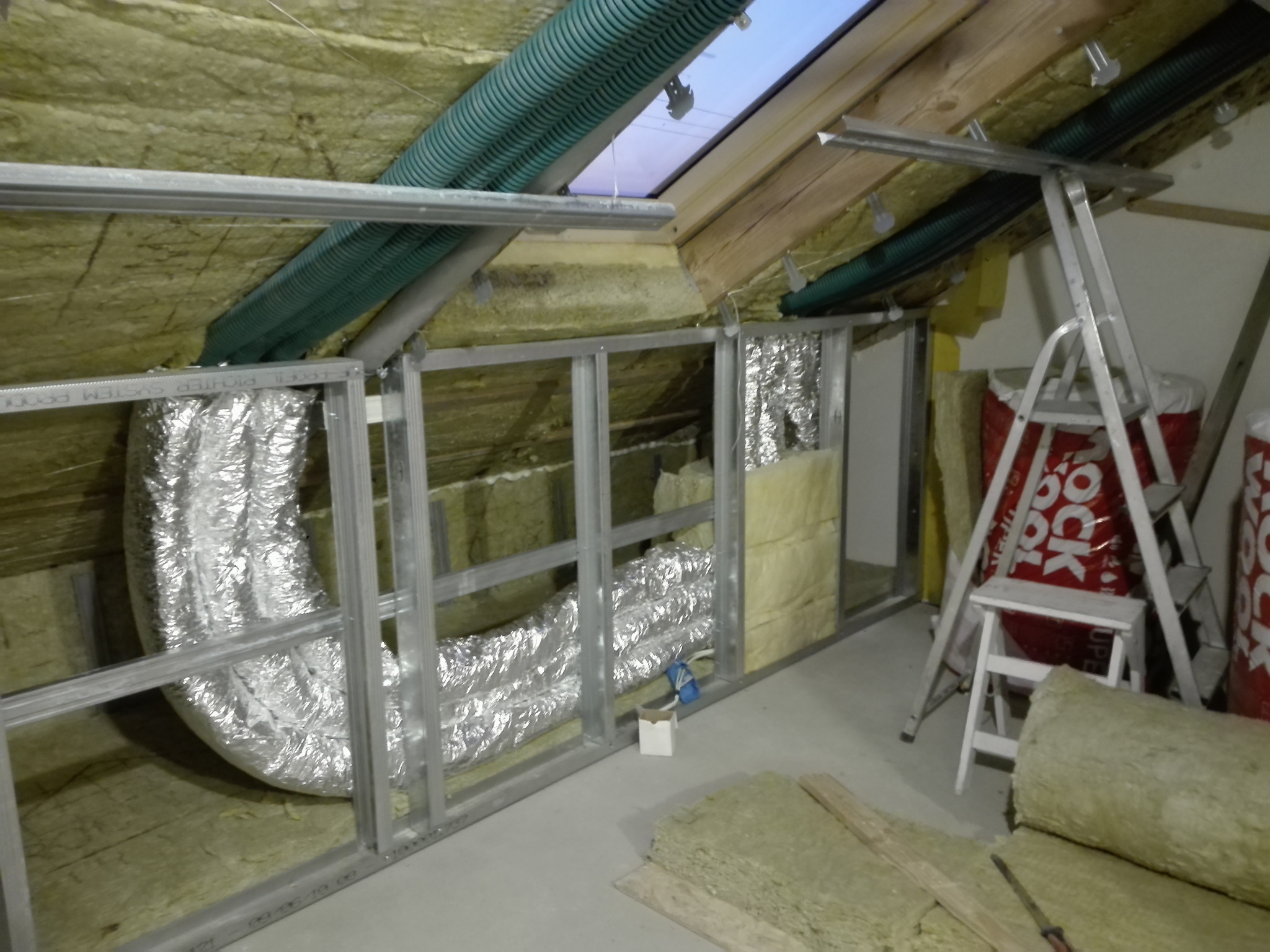 Poddasze w trakcie adaptacji: widoczna instalacja wentylacyjna w srebrnej folii, izolacja z wełny mineralnej i metalowa konstrukcja ścianki działowej.